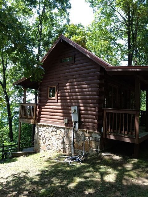 Log cabin with stone foundation and wooden decks, surrounded by trees.