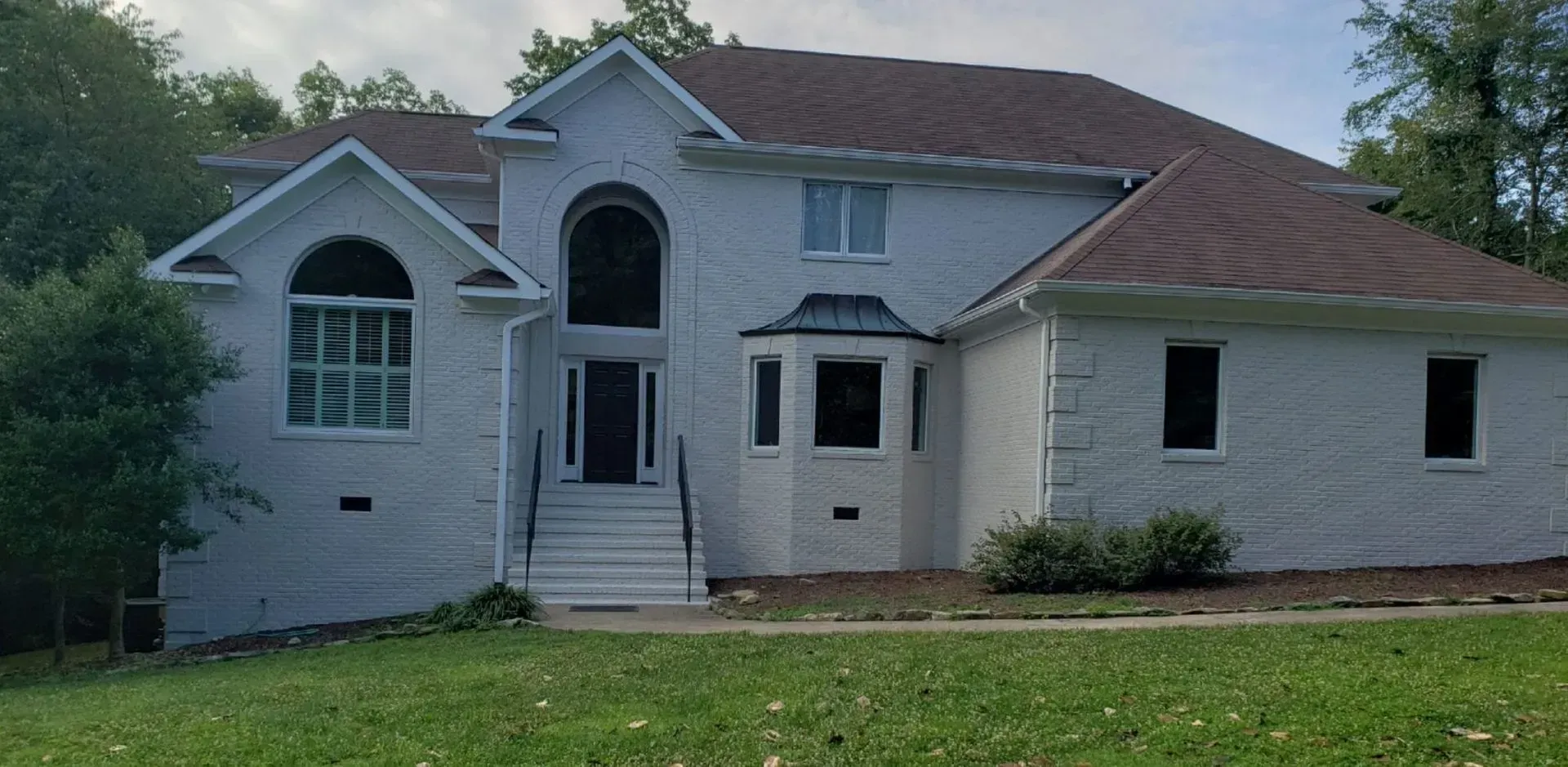 White brick house with brown roof and green lawn.