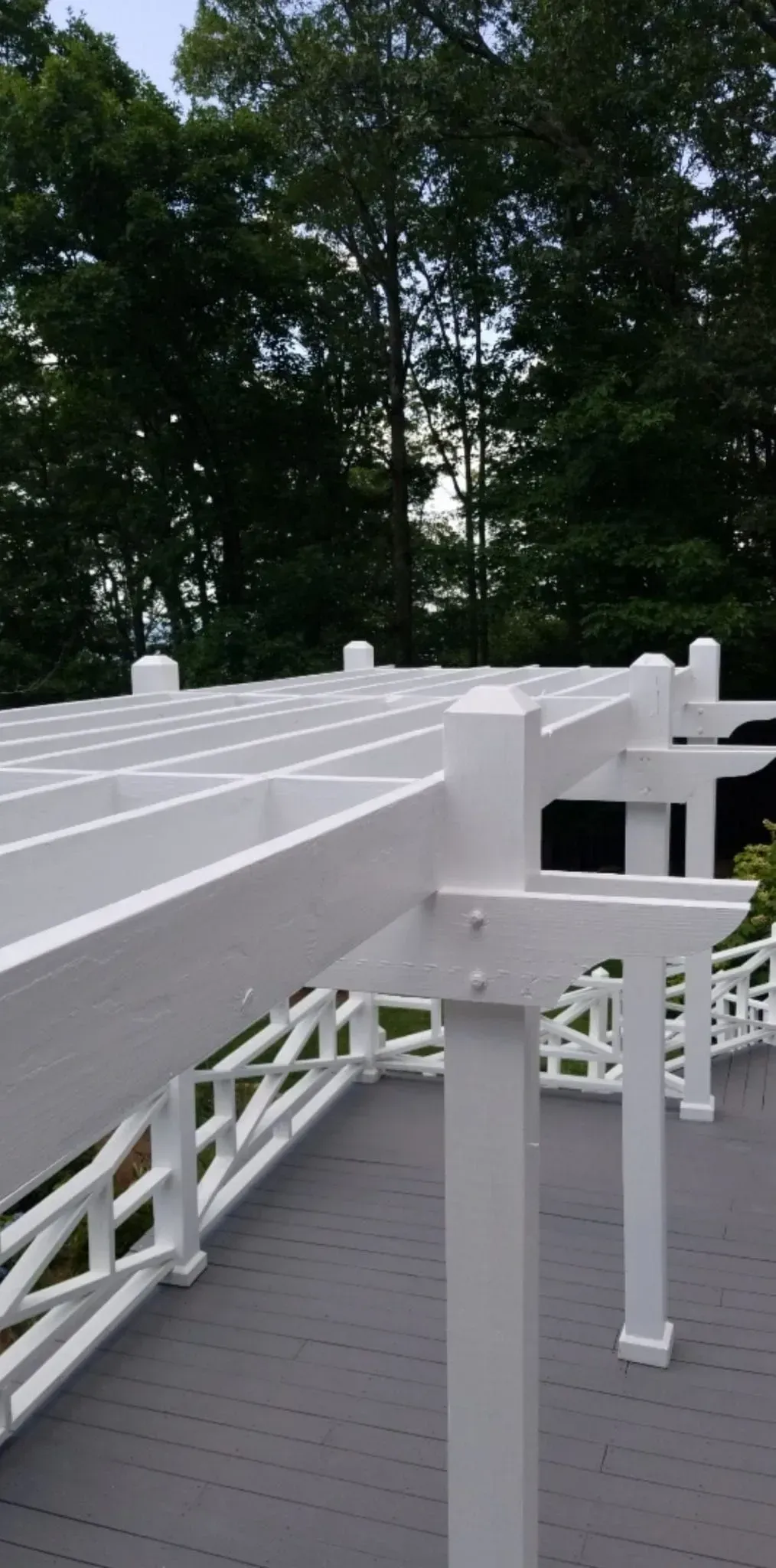 White pergola on a grey deck with a forest backdrop.