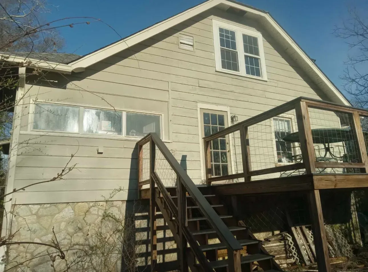 House exterior with wooden deck and stairs. Light siding, stone foundation.