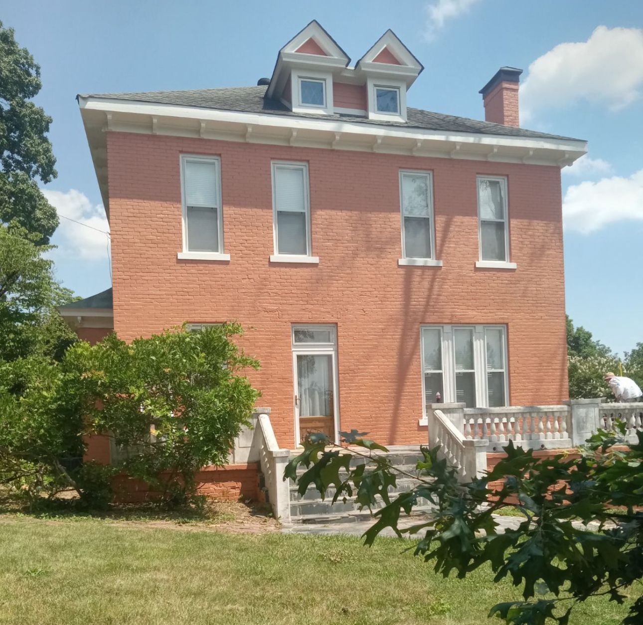 Red brick two-story house with white trim, front steps, and dormer windows under a blue sky.