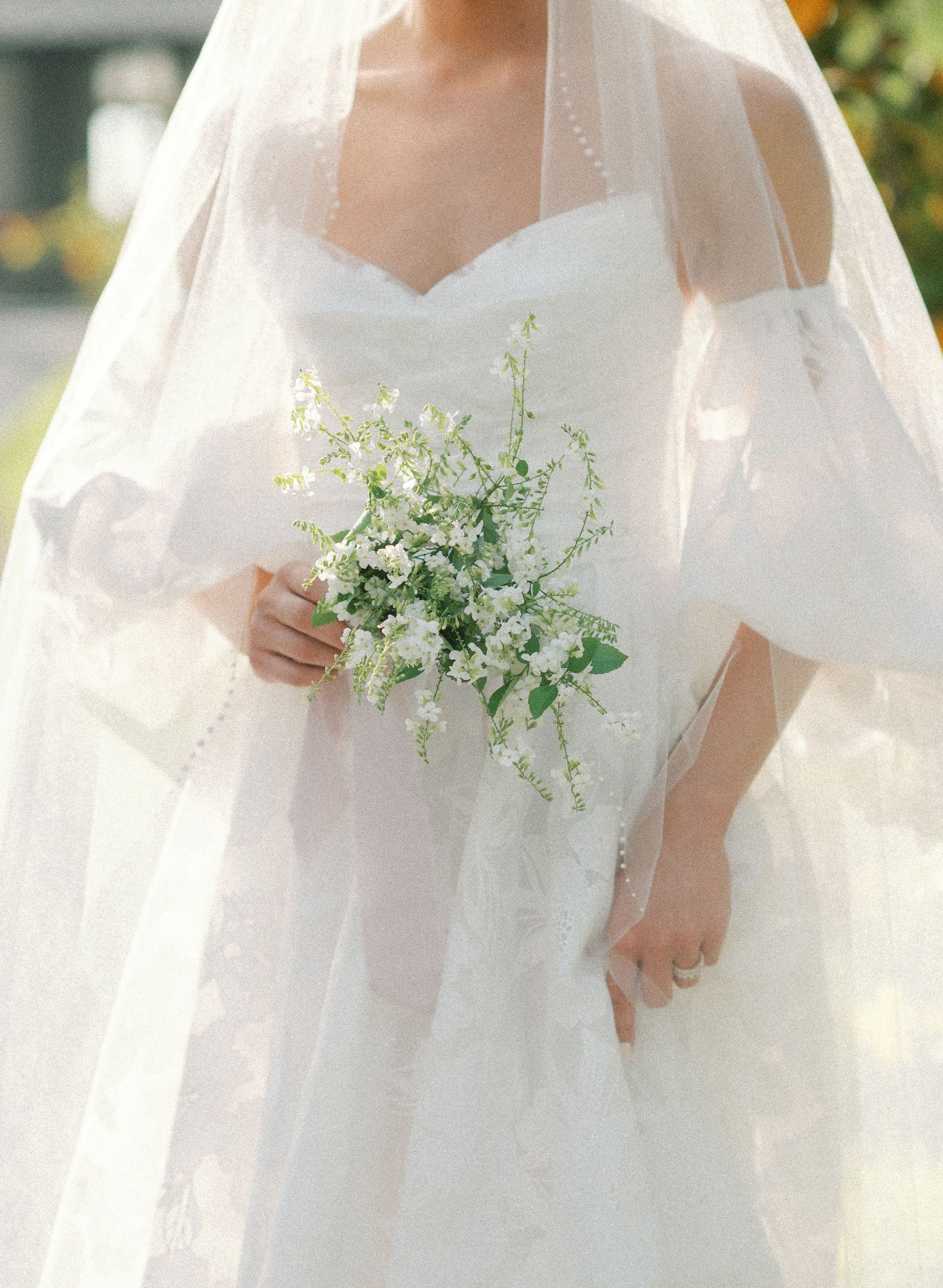 A bride in a white dress and veil is holding a bouquet of white flowers.