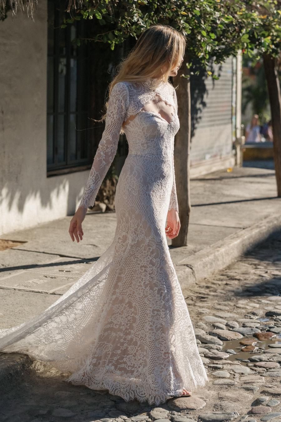 A woman in a white lace dress is standing on a cobblestone street.