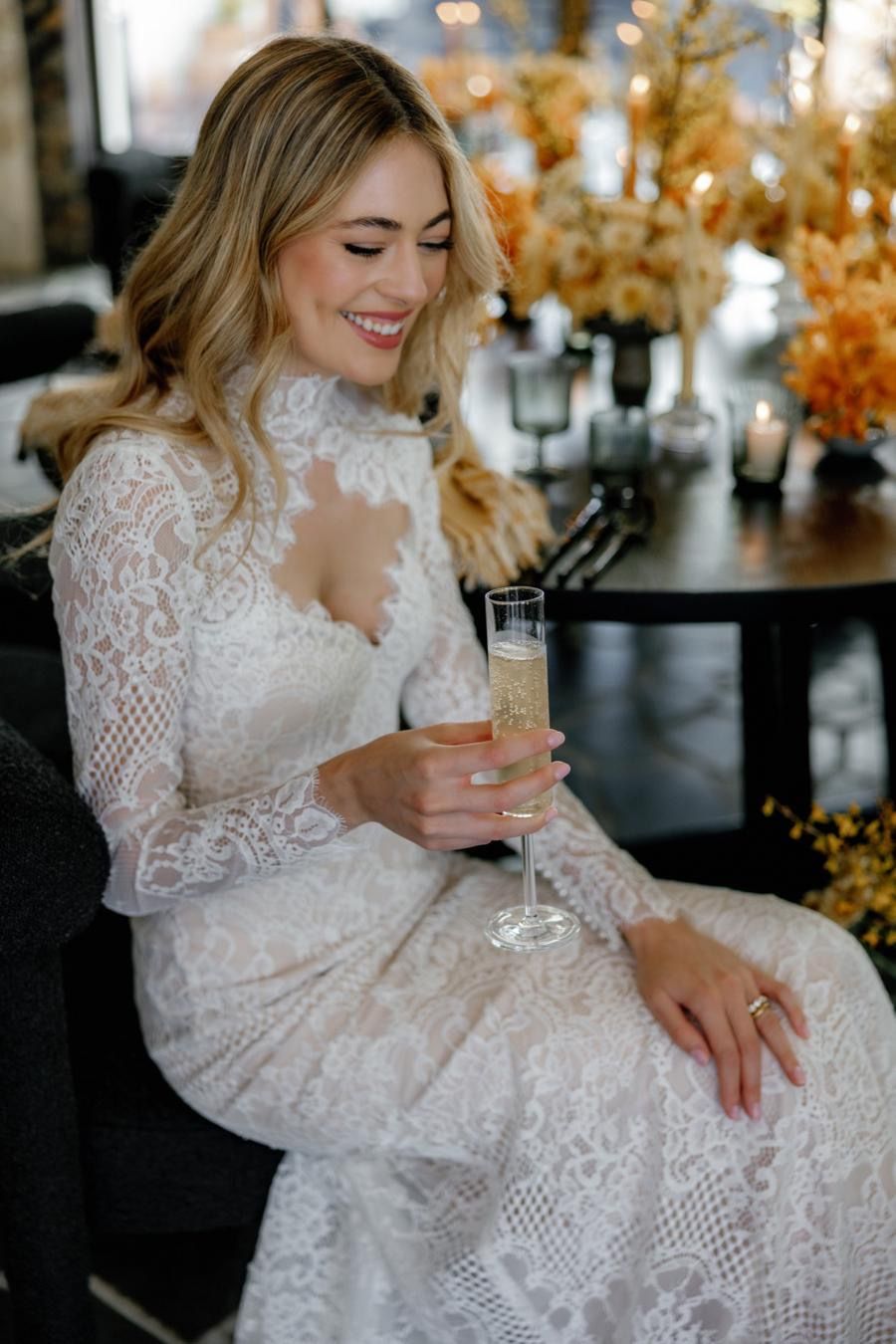 A woman in a wedding dress is sitting in a chair holding a glass of champagne.