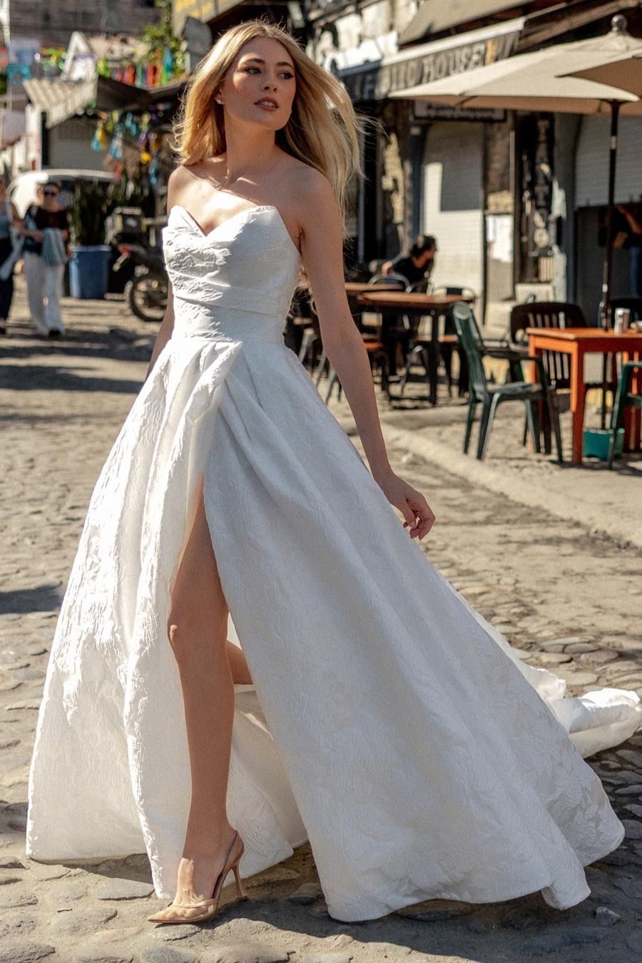 A woman in a white wedding dress is walking down a cobblestone street.
