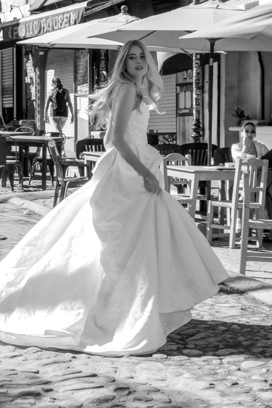 A woman in a wedding dress is walking down a cobblestone street.