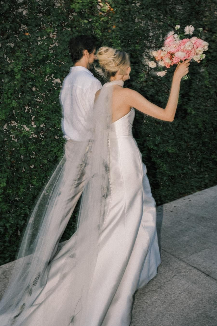 A bride and groom are standing next to each other and the bride is holding a bouquet of pink flowers.