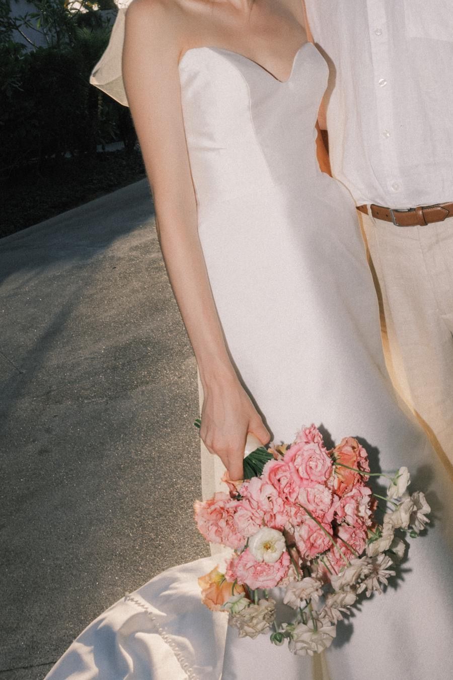A woman in a white dress is holding a bouquet of pink flowers
