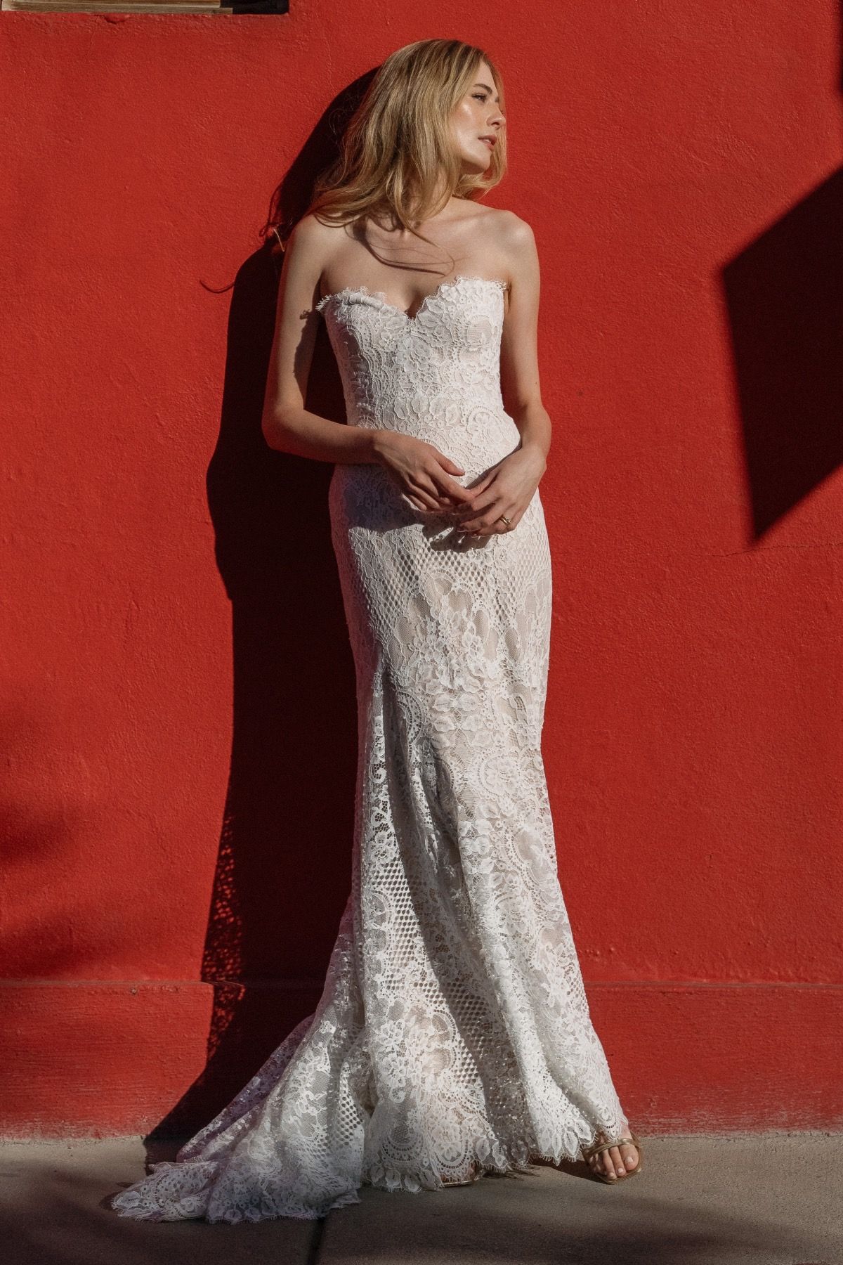 A woman in a white dress is standing in front of a red wall.