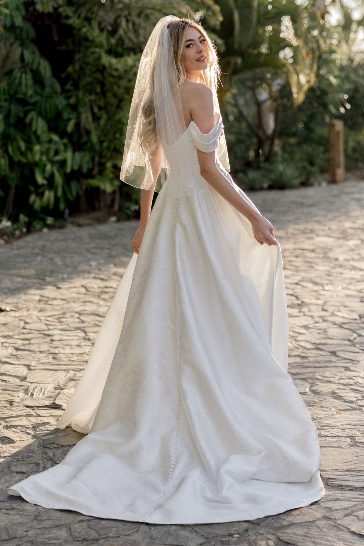 A woman in a wedding dress and veil is standing on a cobblestone road.