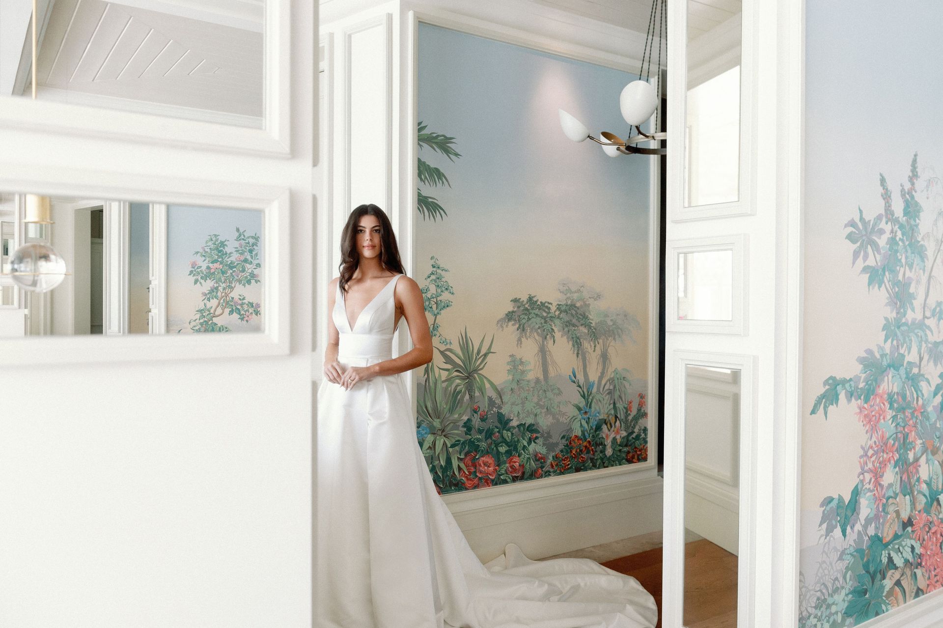 A woman in a wedding dress is standing in front of a painting on the wall.