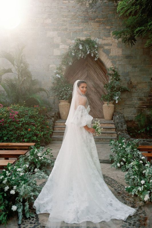 A bride in a wedding dress is standing in front of a stone building holding a bouquet of flowers.