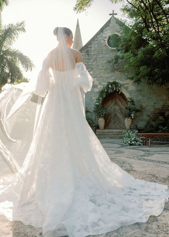 A bride in a wedding dress and veil is standing in front of a church.