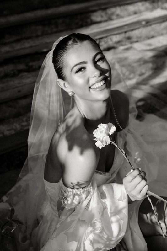 A black and white photo of a bride in a wedding dress holding a flower.
