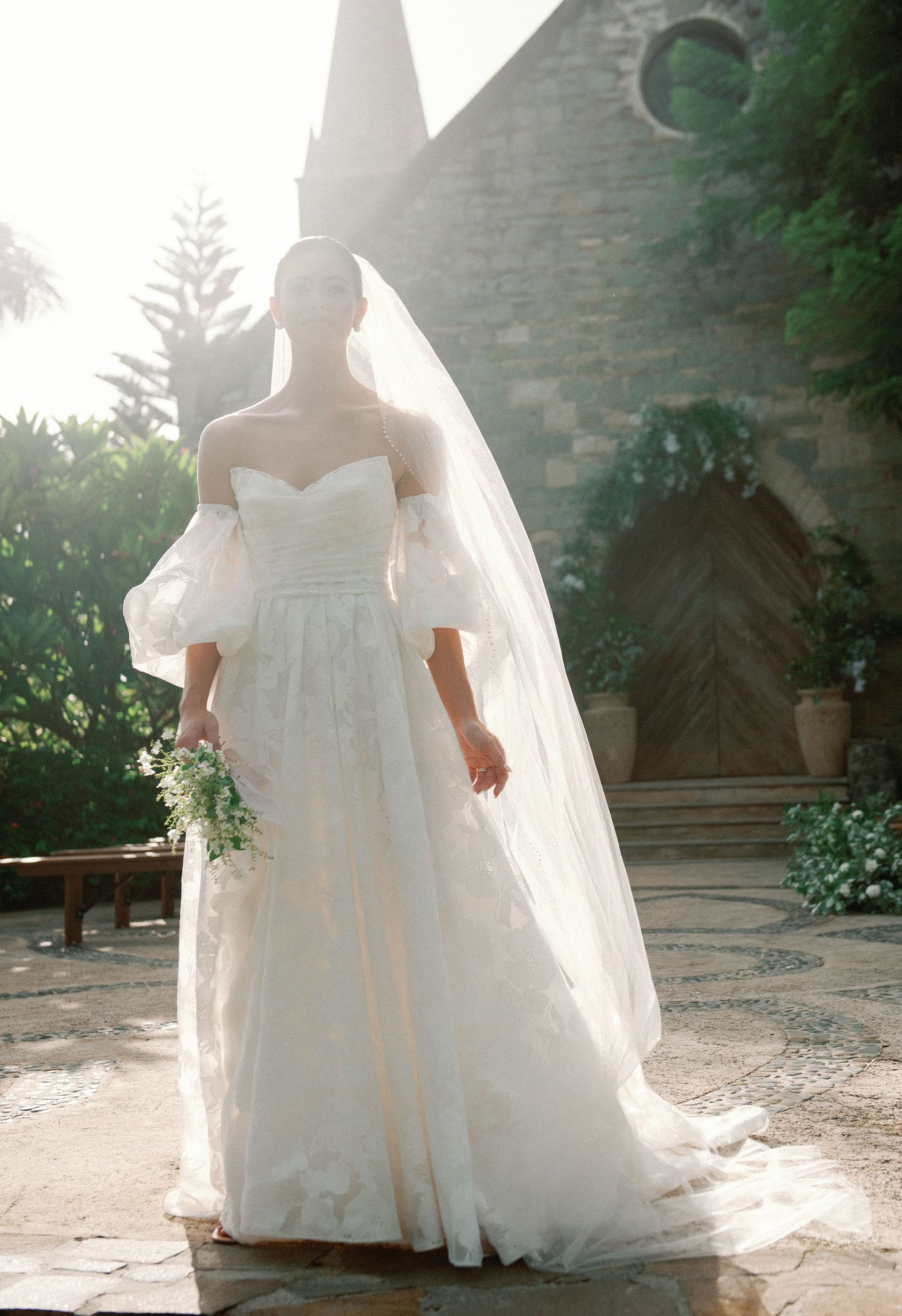 A woman in a wedding dress and veil is standing in front of a church.