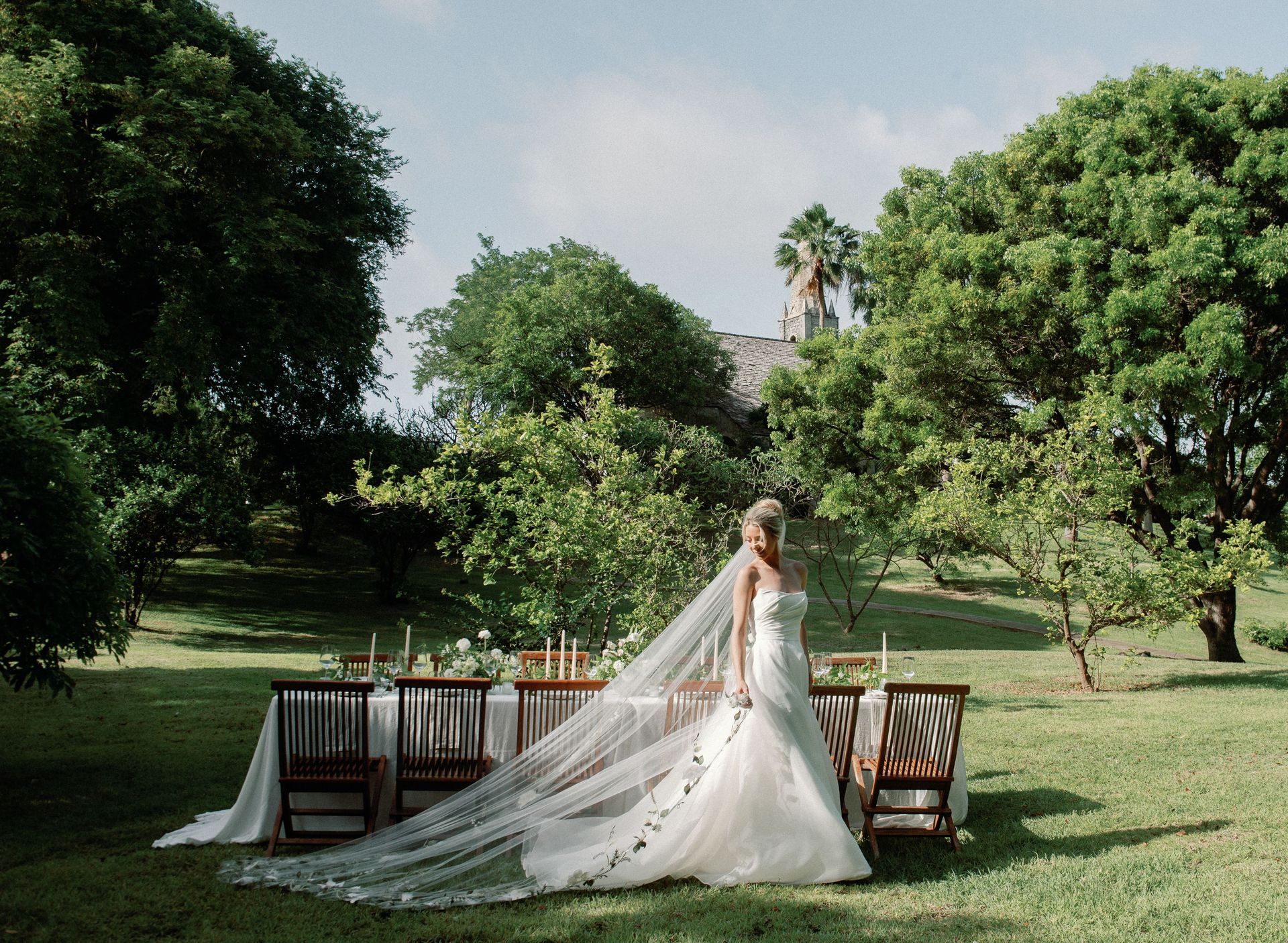 The bride is wearing a long veil and standing in front of a table.