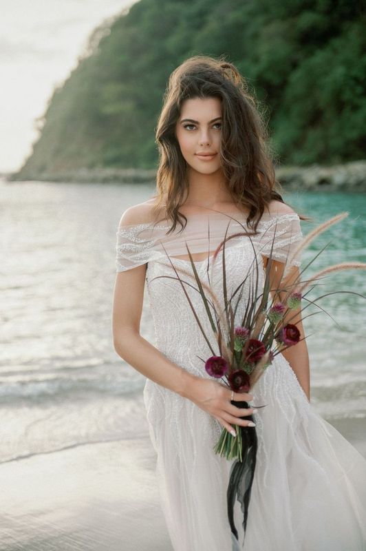 A woman in a wedding dress is holding a bouquet of flowers on the beach.