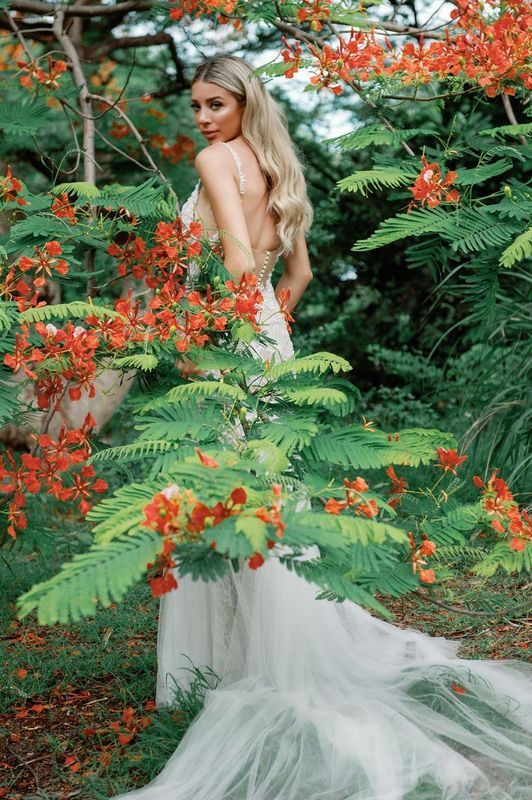 A woman in a wedding dress is standing in a forest surrounded by trees and flowers.
