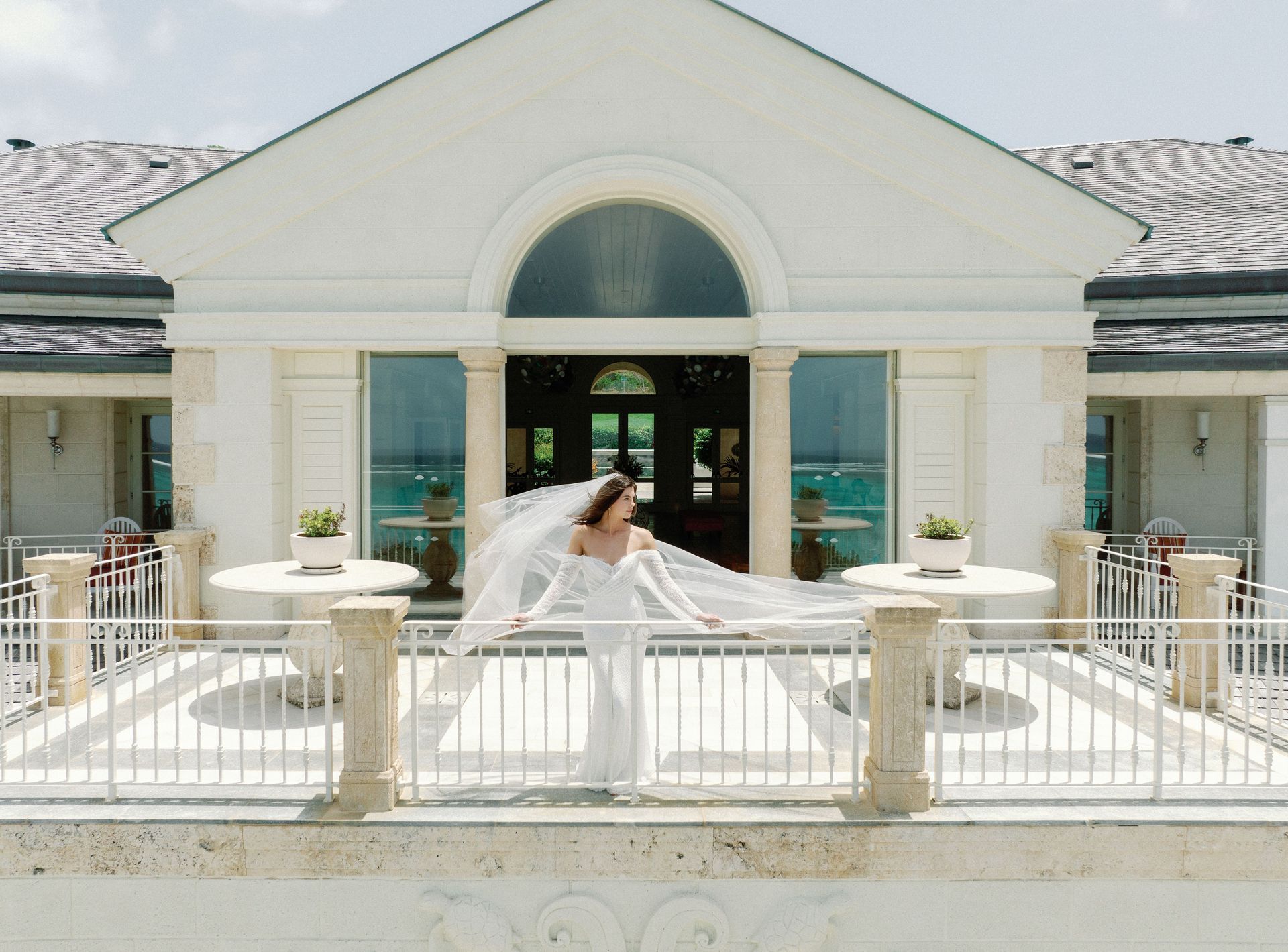 A bride is standing on a balcony in front of a white building.