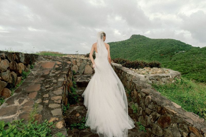 A bride in a wedding dress and veil is walking down a stone wall.