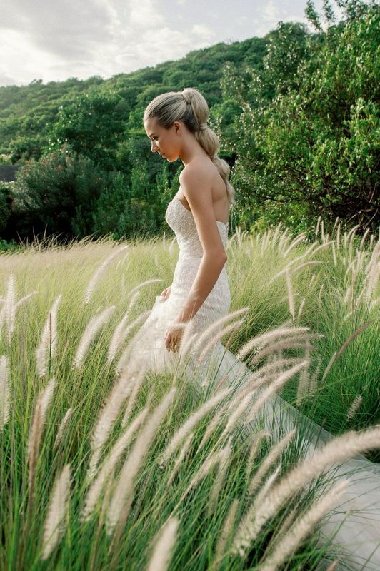 A bride in a wedding dress is walking through a field of tall grass.