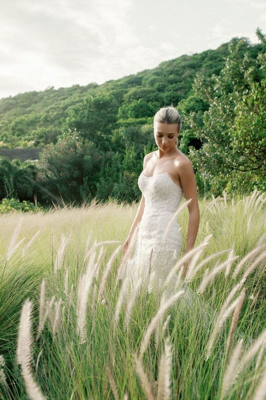 A woman in a wedding dress is standing in a field of tall grass.