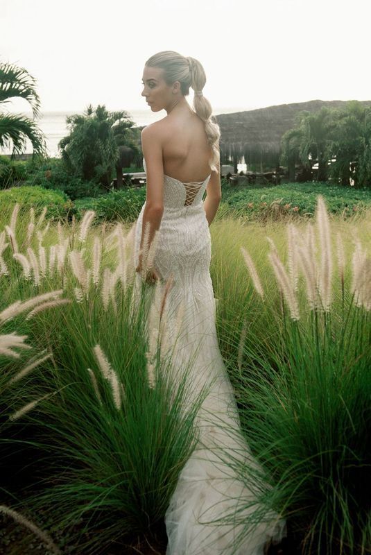 A woman in a wedding dress is standing in a field of tall grass.