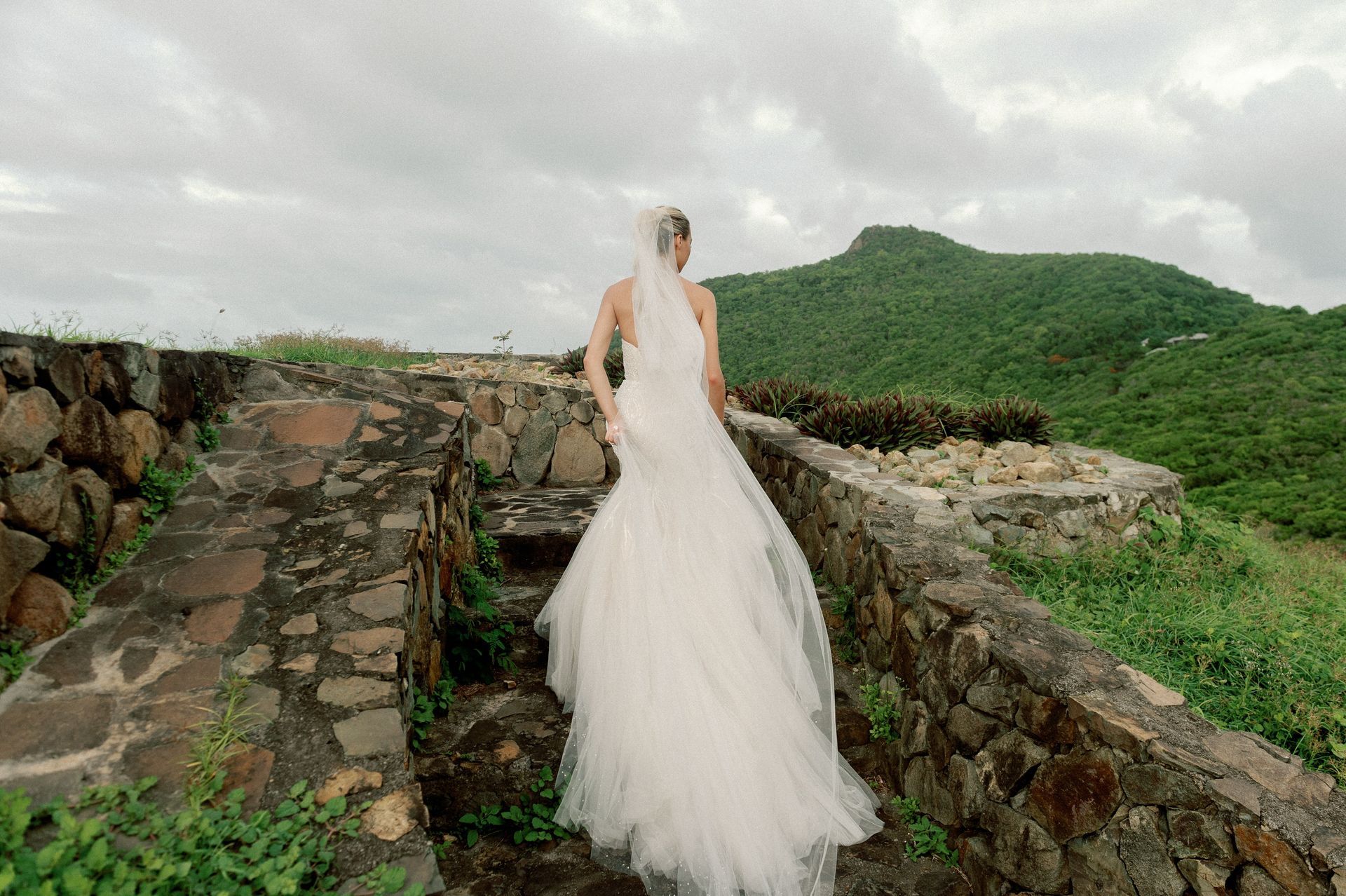 A bride in a wedding dress is walking down a stone wall.