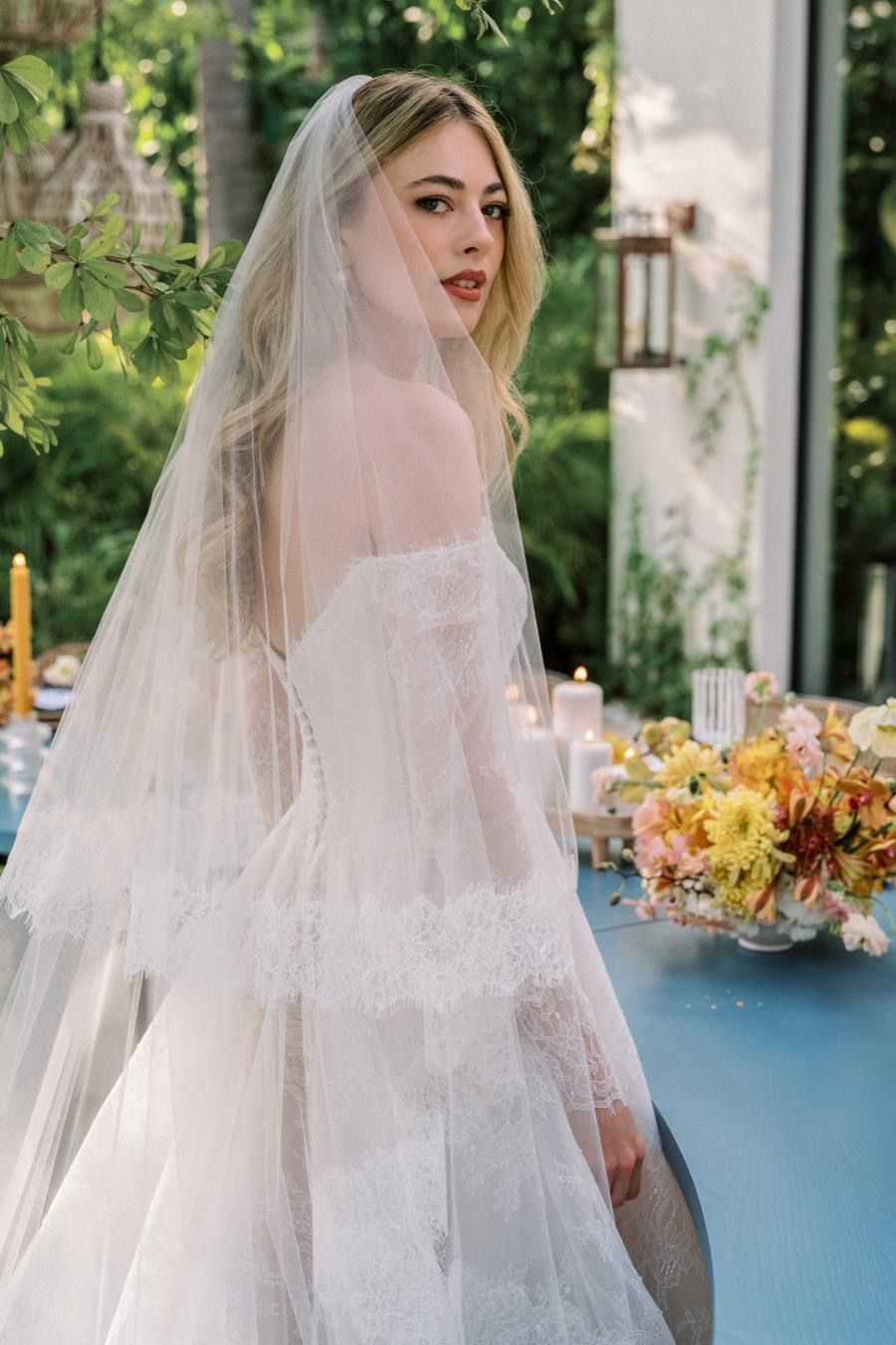 A woman in a wedding dress and veil is standing in front of a table.