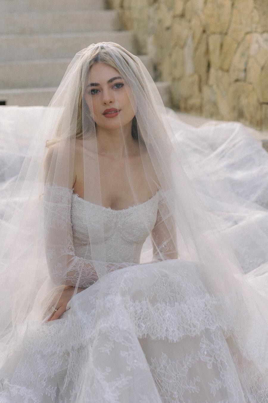 A woman in a wedding dress and veil is sitting on a set of stairs.