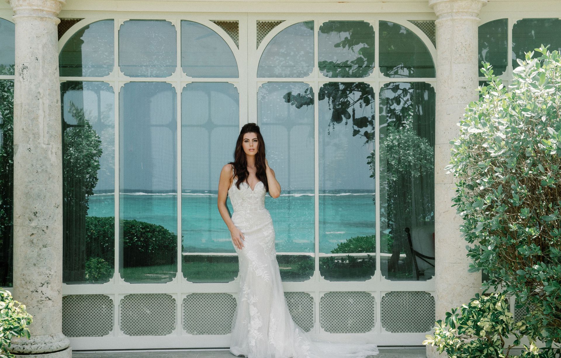 A woman in a wedding dress is standing in front of a large window.
