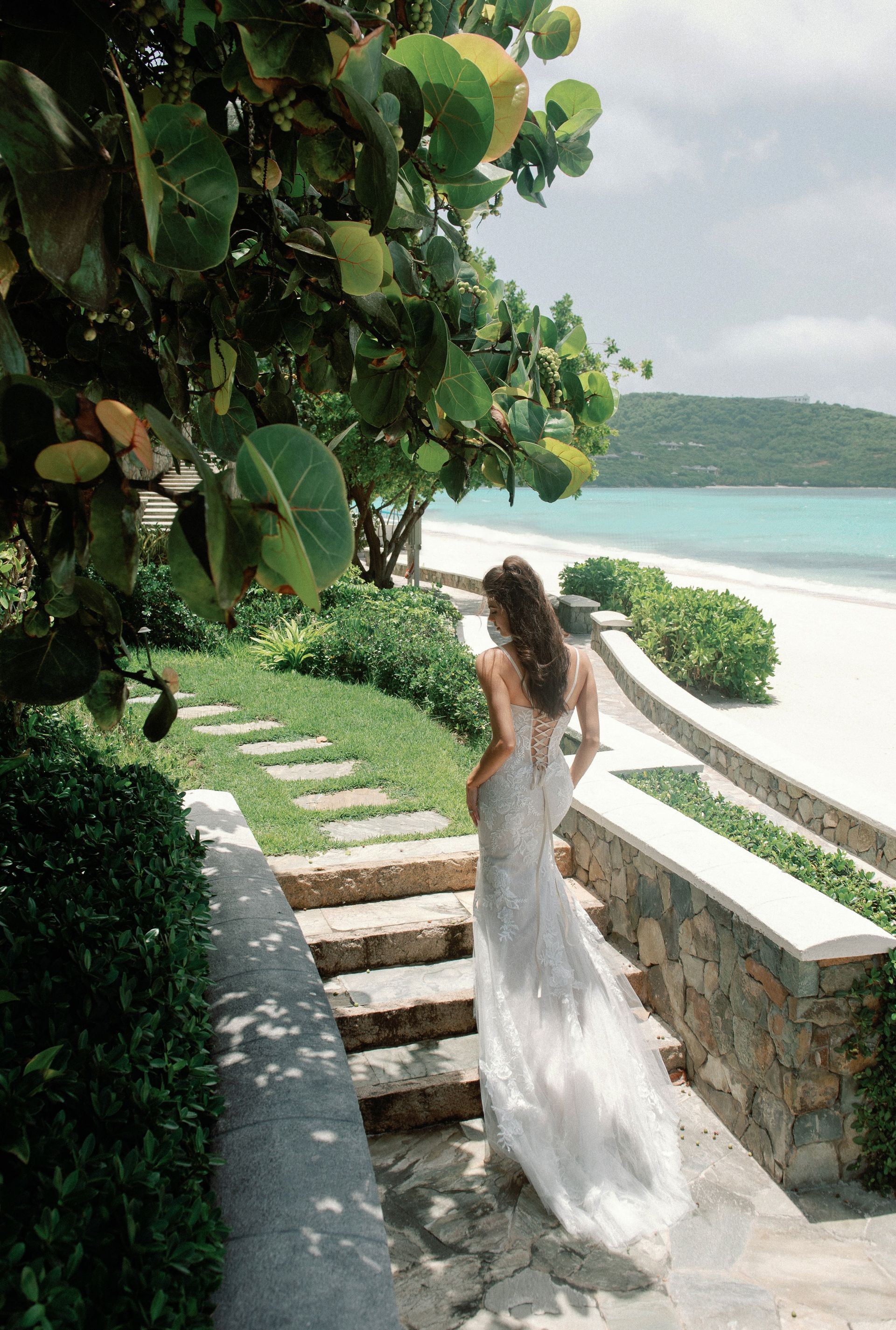 A woman in a wedding dress is walking down stairs to the beach.
