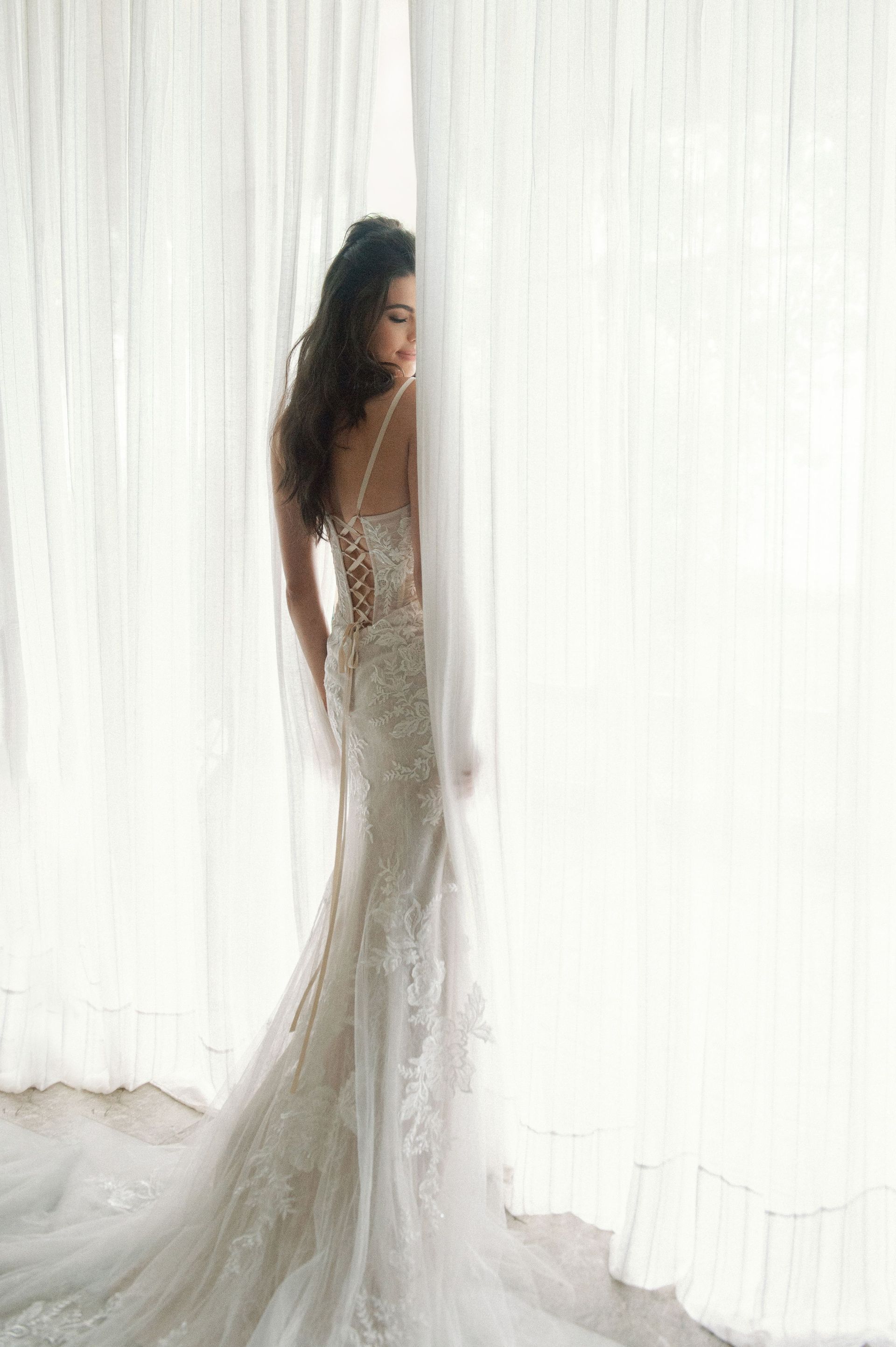 A woman in a wedding dress is standing in front of a window.