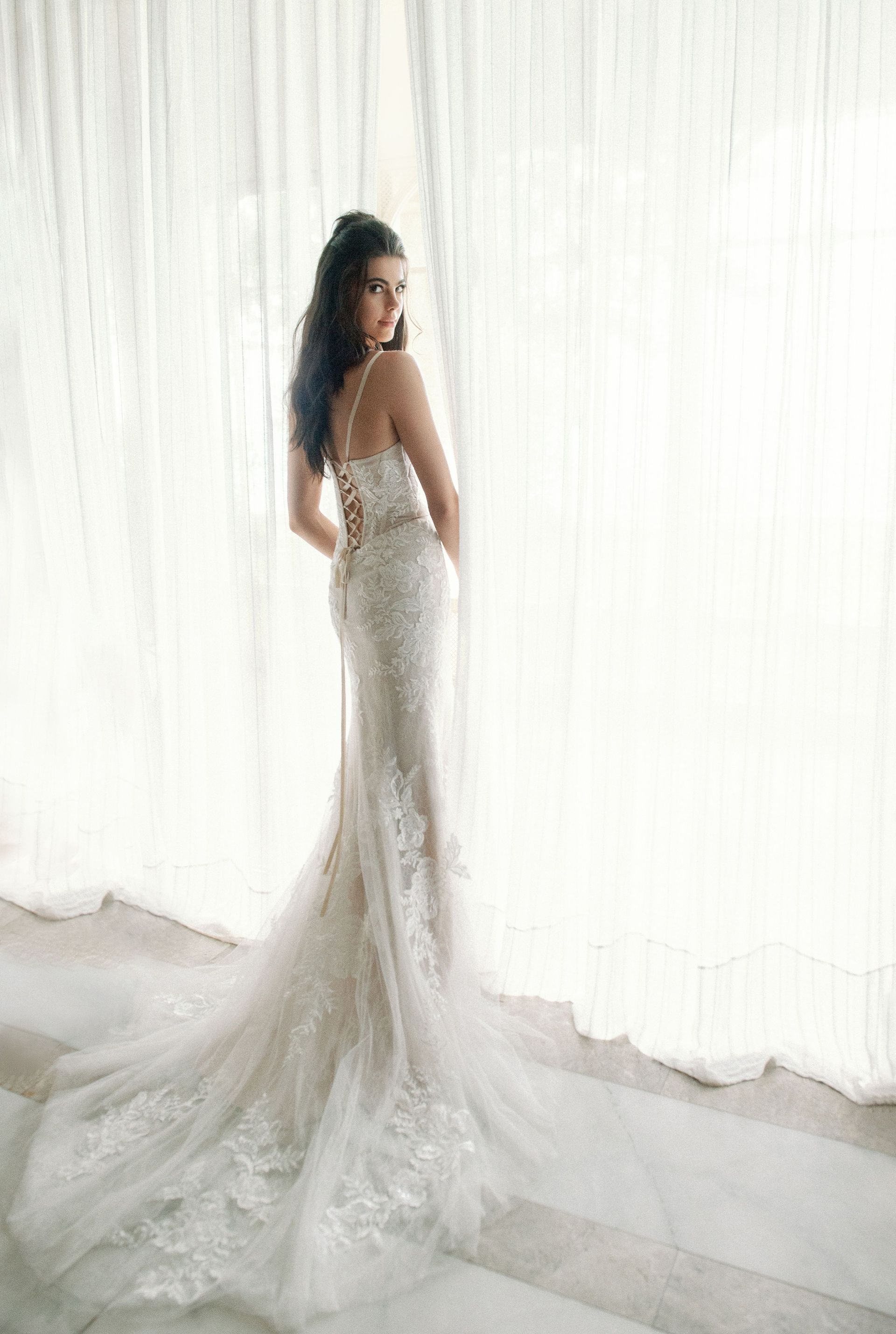 A woman in a wedding dress is standing in front of a window.