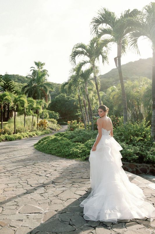 A bride in a wedding dress is walking down a path surrounded by palm trees.