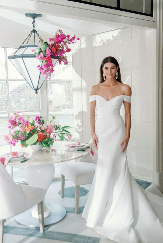 A woman in a white dress is standing in a room next to a table and chairs.