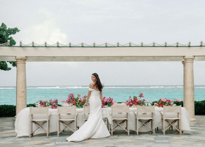 A bride in a white dress is standing in front of a long table.