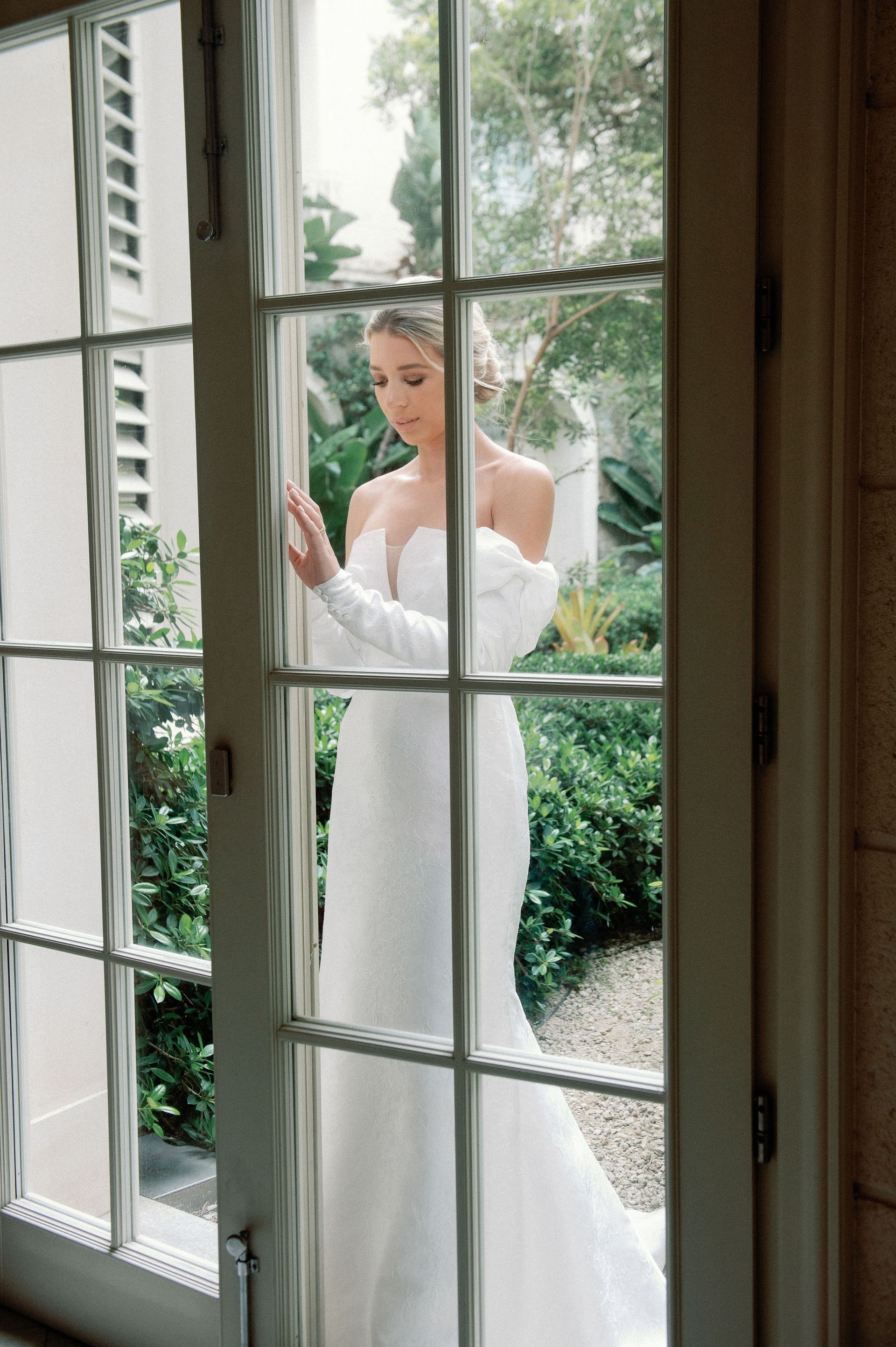 A woman in a white dress is standing in front of a window.