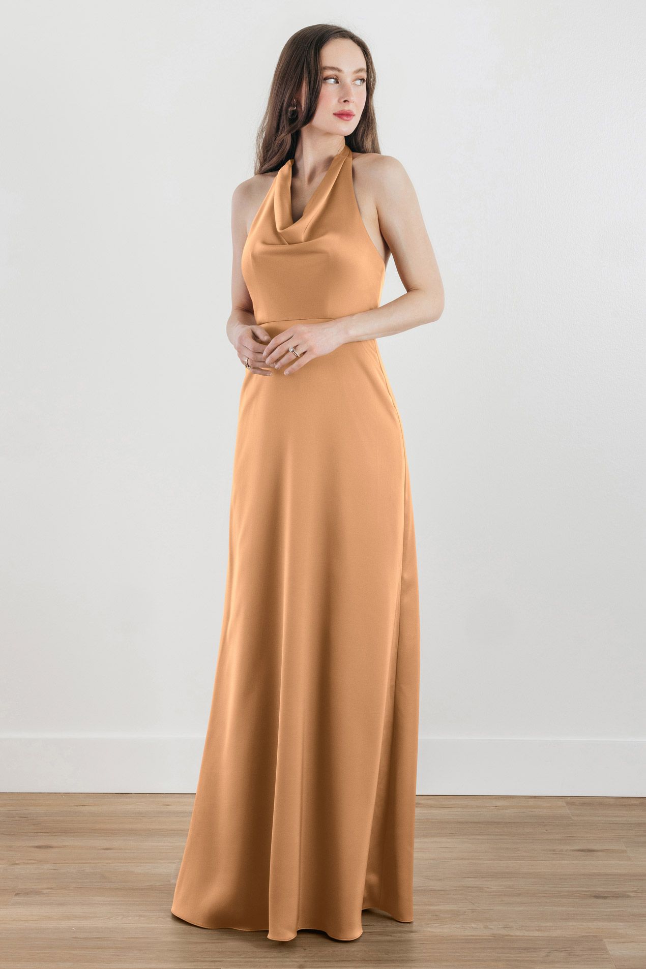 A woman in a long orange dress is standing on a wooden floor.