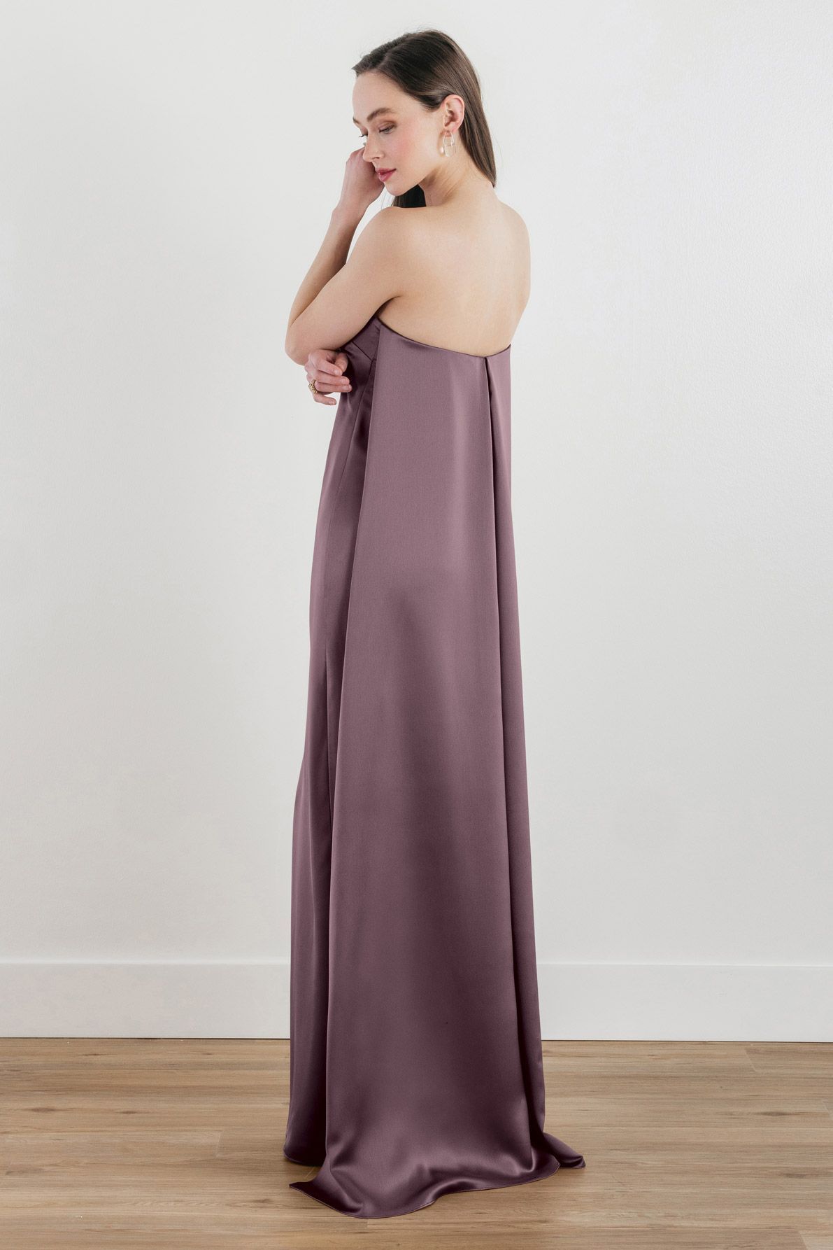 A woman is wearing a purple strapless dress and standing on a wooden floor.