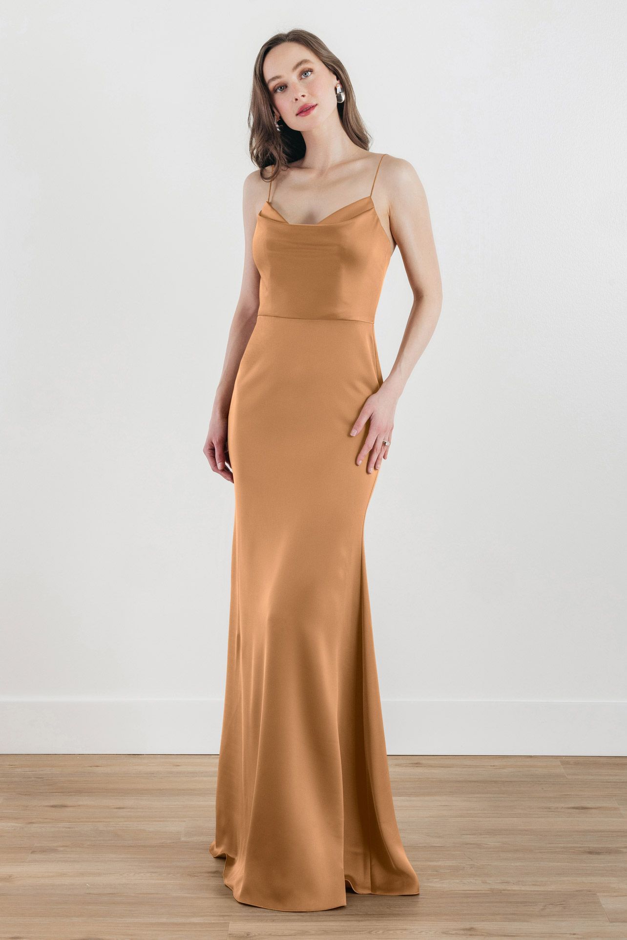 A woman in a long brown dress is standing on a wooden floor.