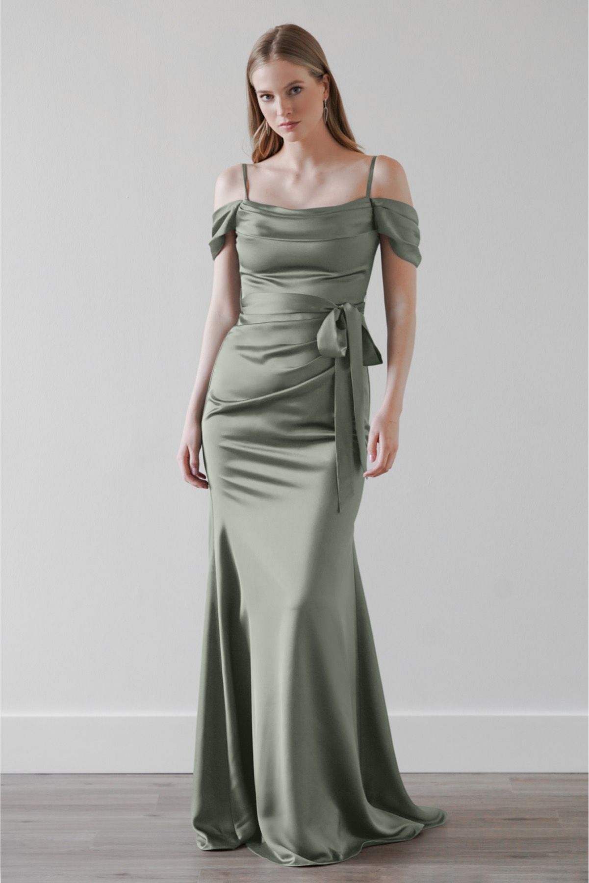 A woman is wearing a green satin off the shoulder bridesmaid dress.