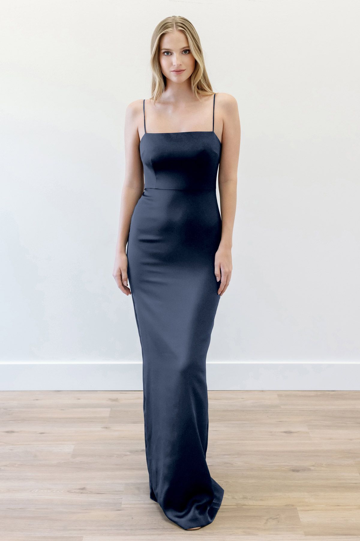 A woman in a long black dress is standing on a wooden floor.