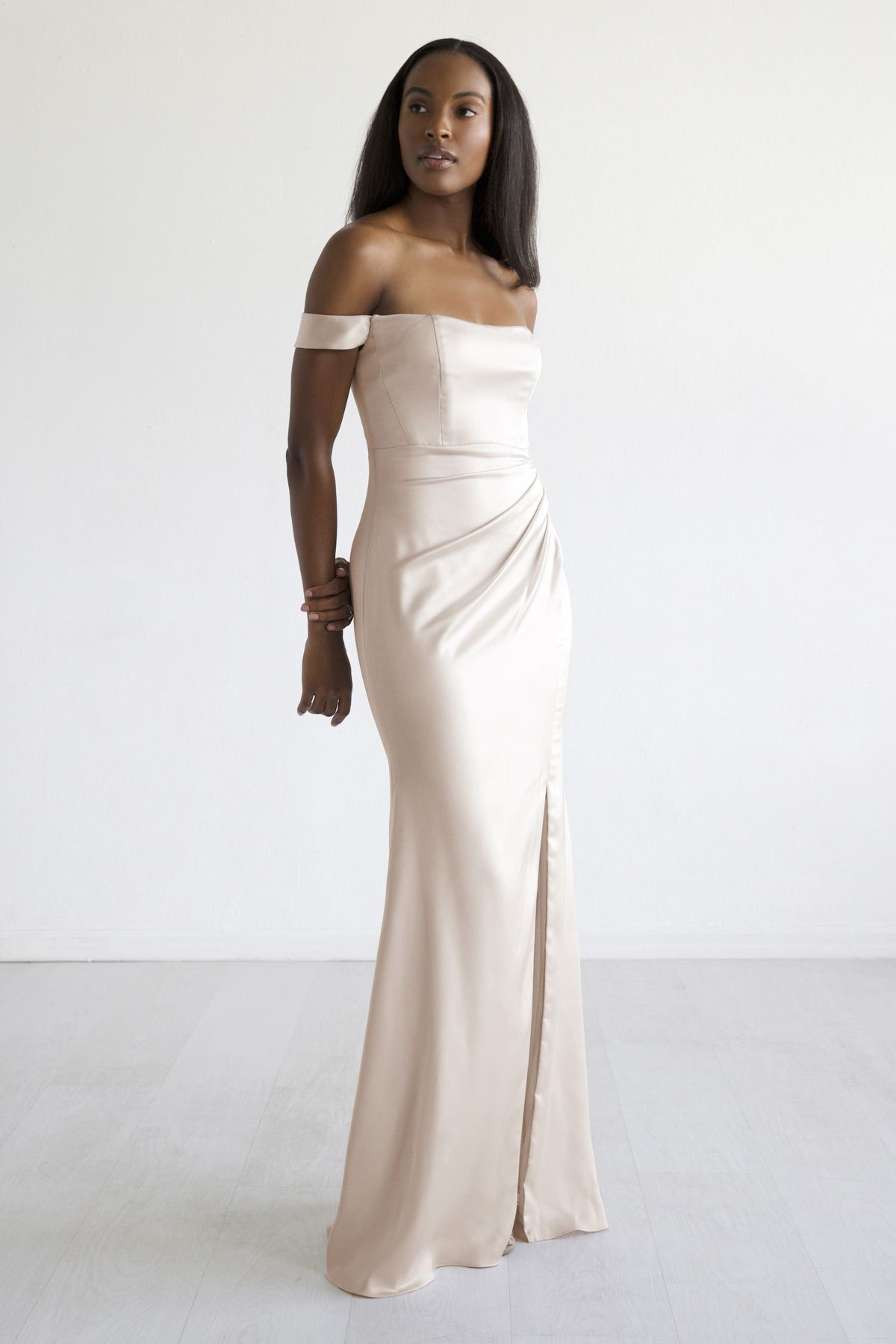 A woman in a long white dress is standing in front of a white wall.