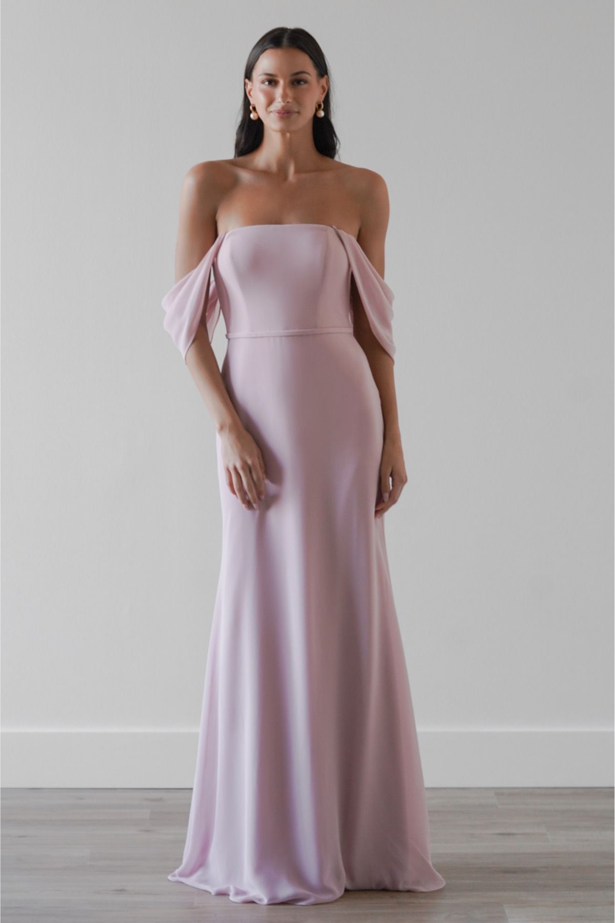 A woman is wearing a pink off the shoulder bridesmaid dress.