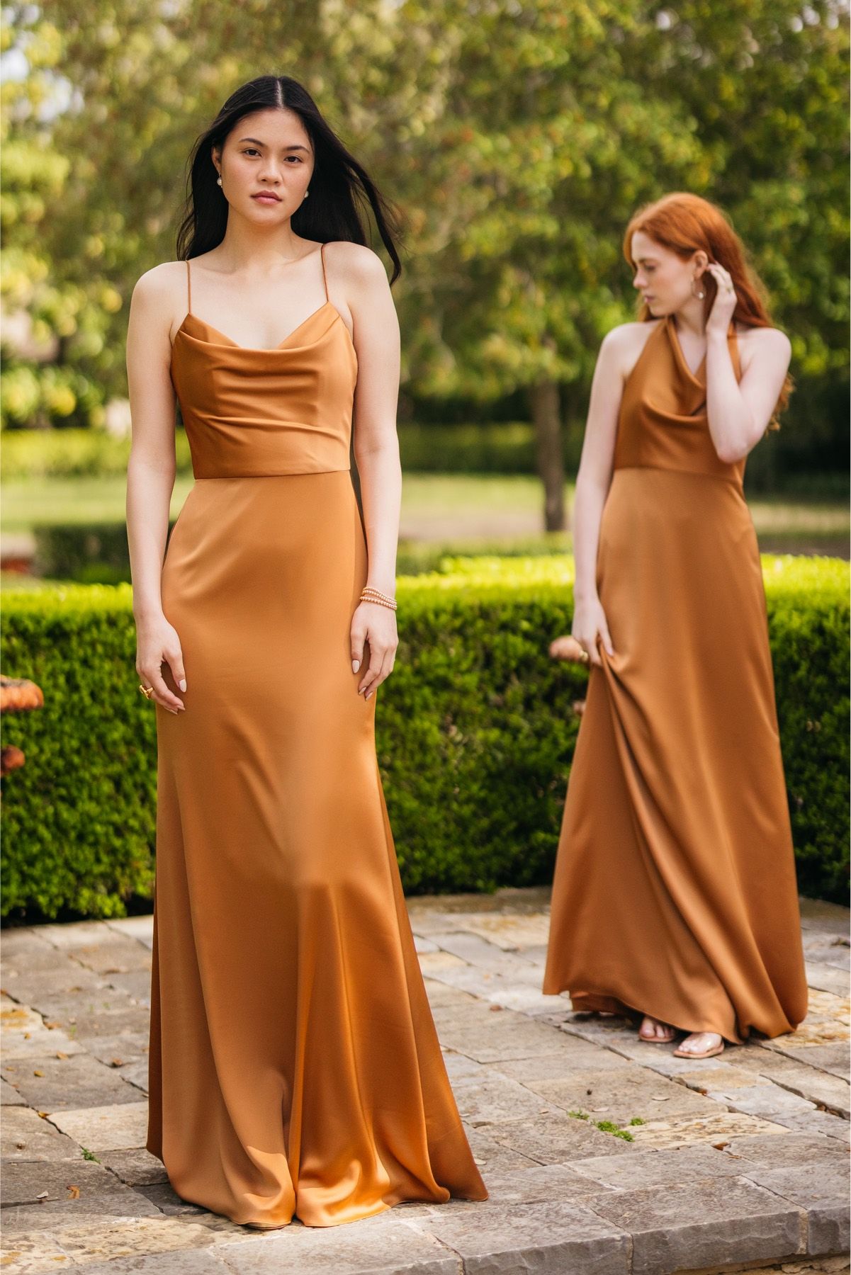 Two women in long brown dresses are standing next to each other on a sidewalk.