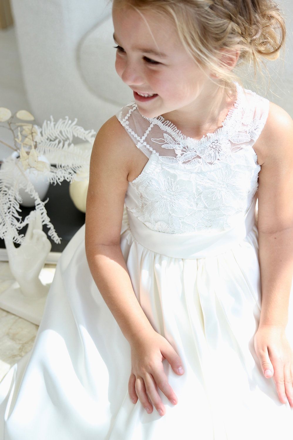 A little girl is wearing a white dress and smiling.