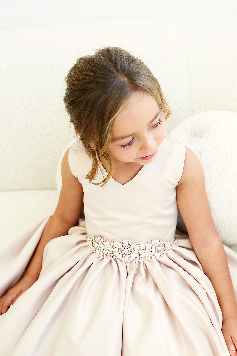 A little girl in a white dress is sitting on a couch.