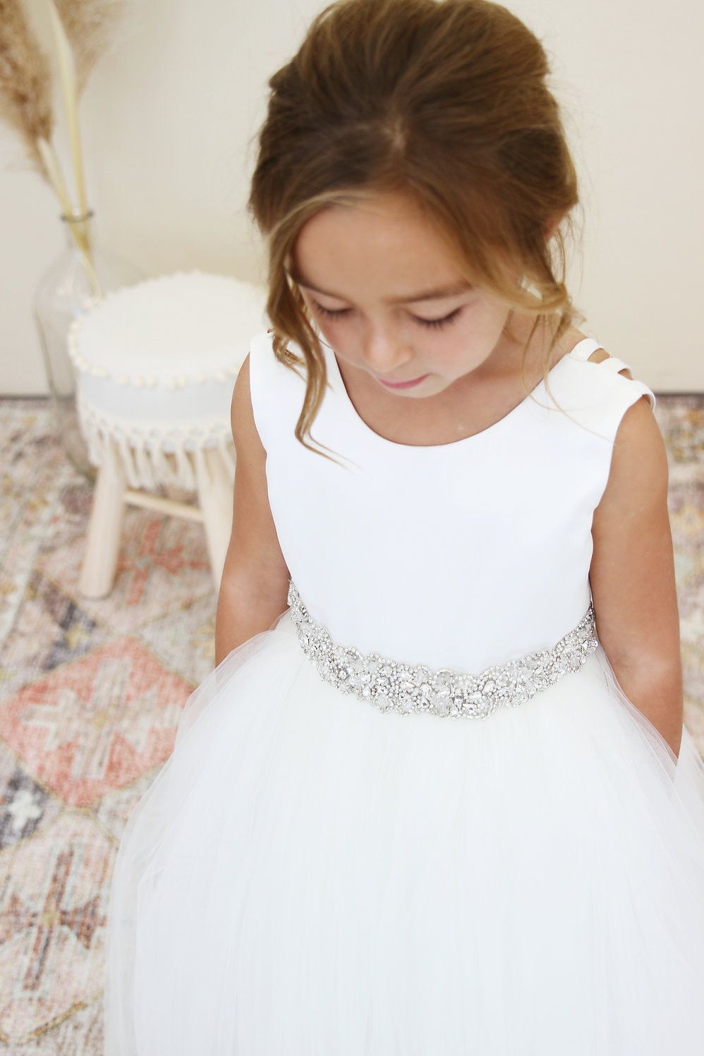 A little girl is wearing a white dress with a rhinestone belt.