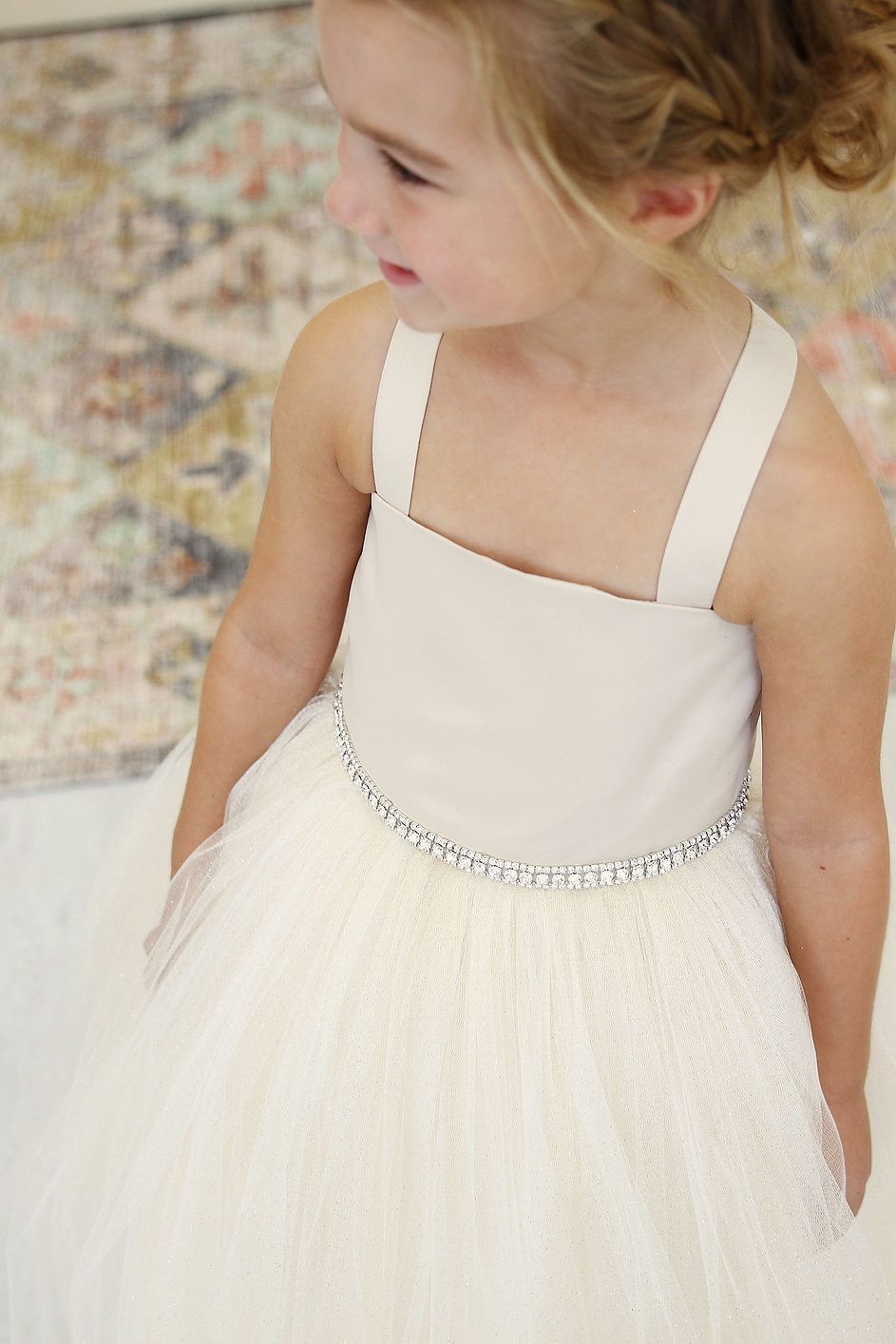 A little girl is wearing a white dress with a rhinestone belt.